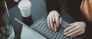 Hands typing on a keyboard beside a coffee cup